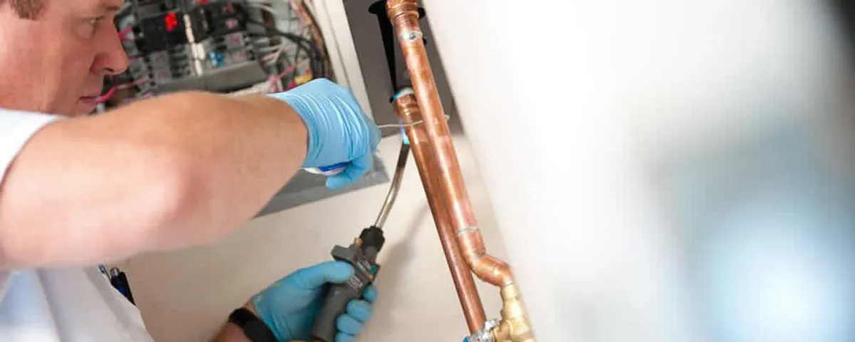 Water heater repair technician testing copper pipe connections and controls in El Paso, TX