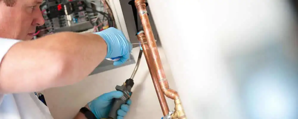 Water heater repair technician testing copper pipe connections and controls in El Paso, TX